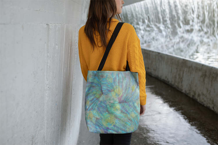 Person holding a colorful tote bag by a water feature