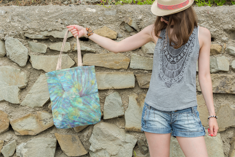 Woman holding a tie-dye bag against a stone wall