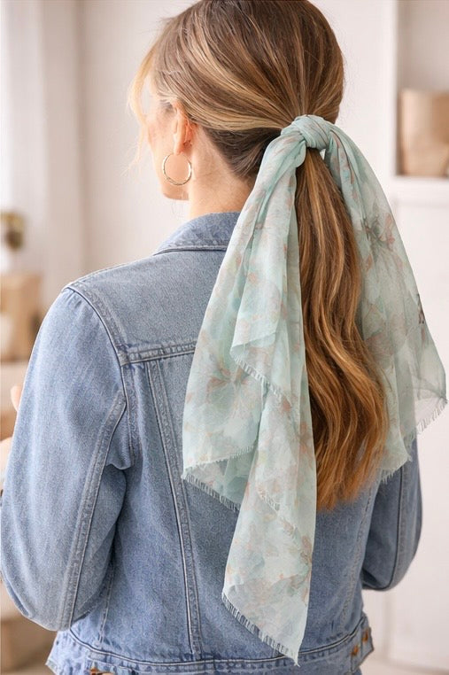 Person wearing a light blue denim jacket with a floral scarf tied around their ponytail.