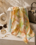 Colorful scarf draped over a surface with a vase, sunglasses, and handbag in the background.